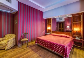 Camera d'albergo con un letto grande, una sedia, un comodino e uno specchio.
