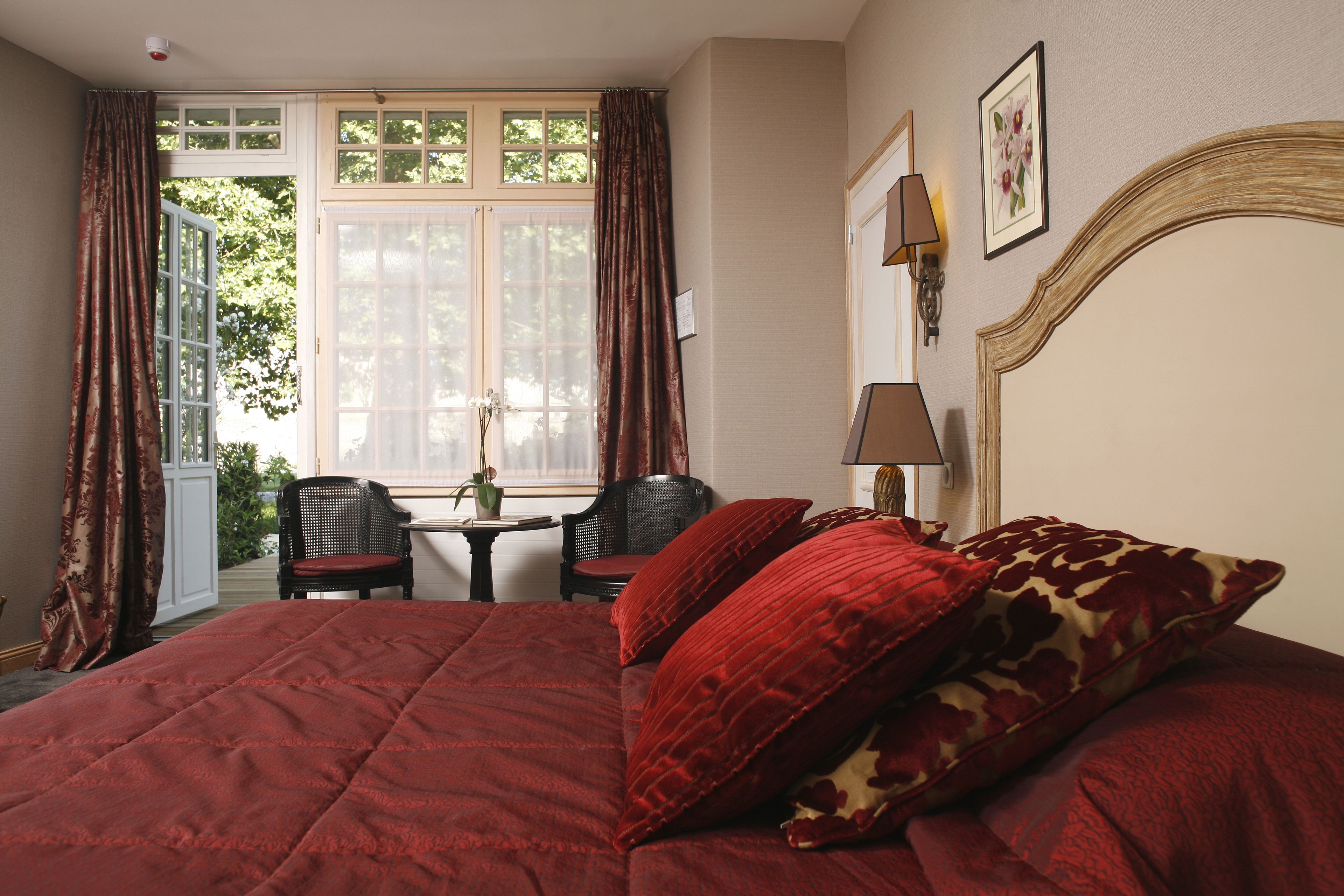 A bedroom with a large bed, two chairs, a small table, and a window with curtains.