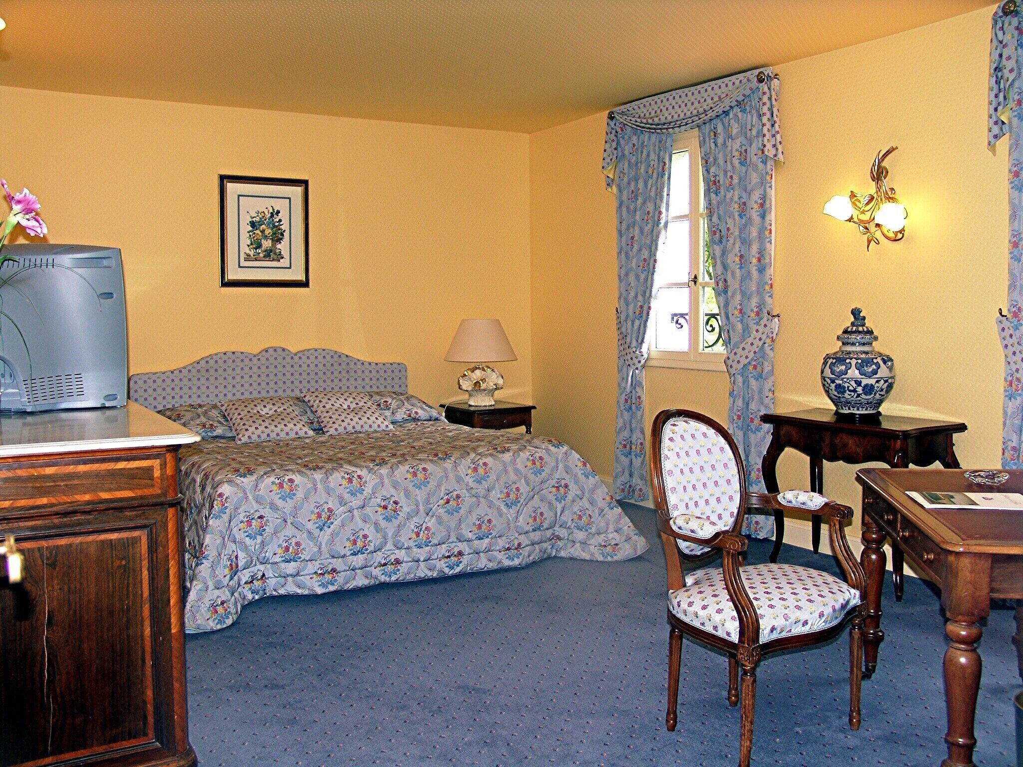 Une chambre à coucher avec un lit, un bureau, une chaise, une lampe, un vase et un tableau au mur.
