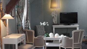 A modern hotel room with a television, a desk, two chairs, a lamp, and decorative items.