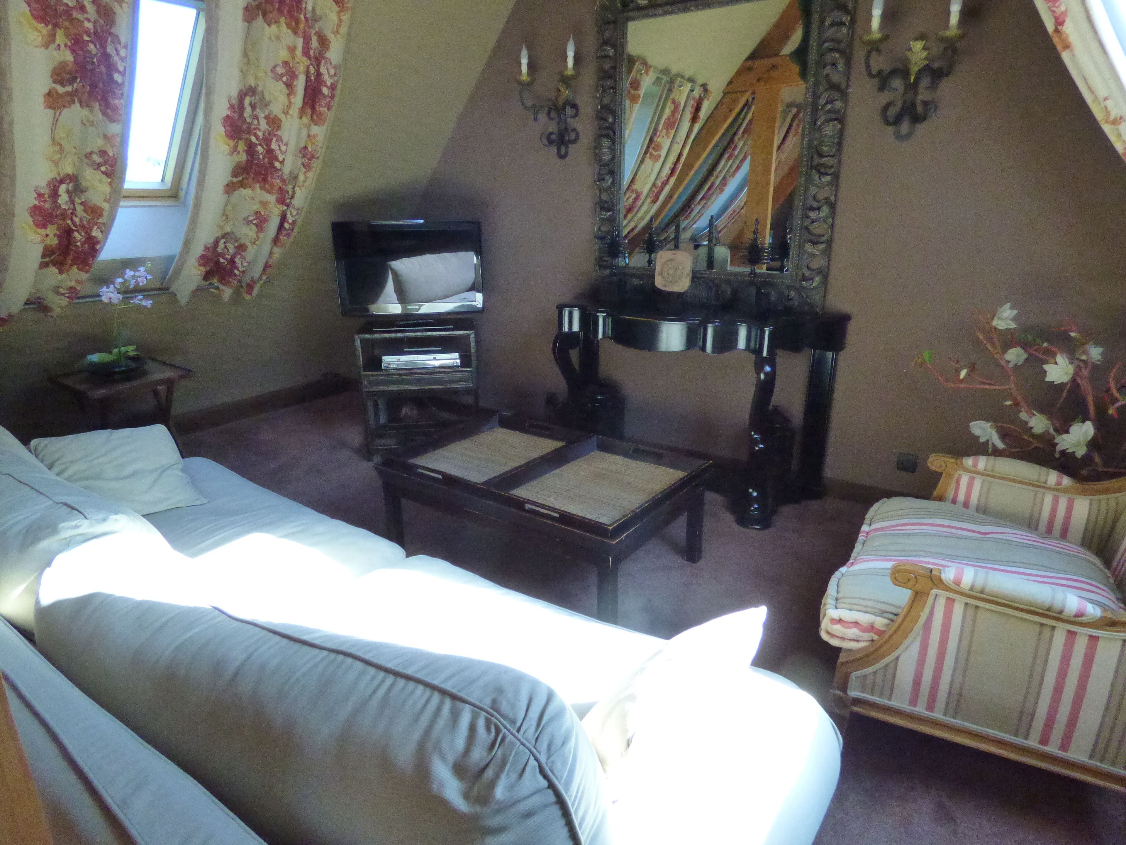 Una sala de estar con un sofá, una silla, una mesita, un televisor y un espejo.