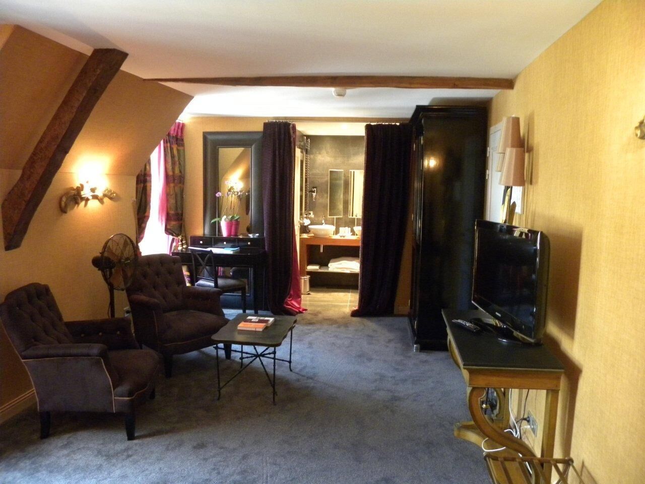 A cozy living room with a sofa, armchairs, a coffee table, and a television. A staircase leads to a bathroom with a mirror and sink.