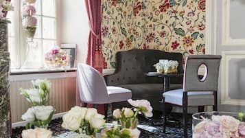 Une pièce avec un papier peint à motifs floraux, un canapé, deux fauteuils, une petite table et un vase rempli de fleurs.