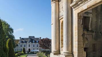 Un bâtiment de style classique, doté de colonnes et agrémenté d’un jardin bien entretenu qui mène à une grande et imposante demeure.