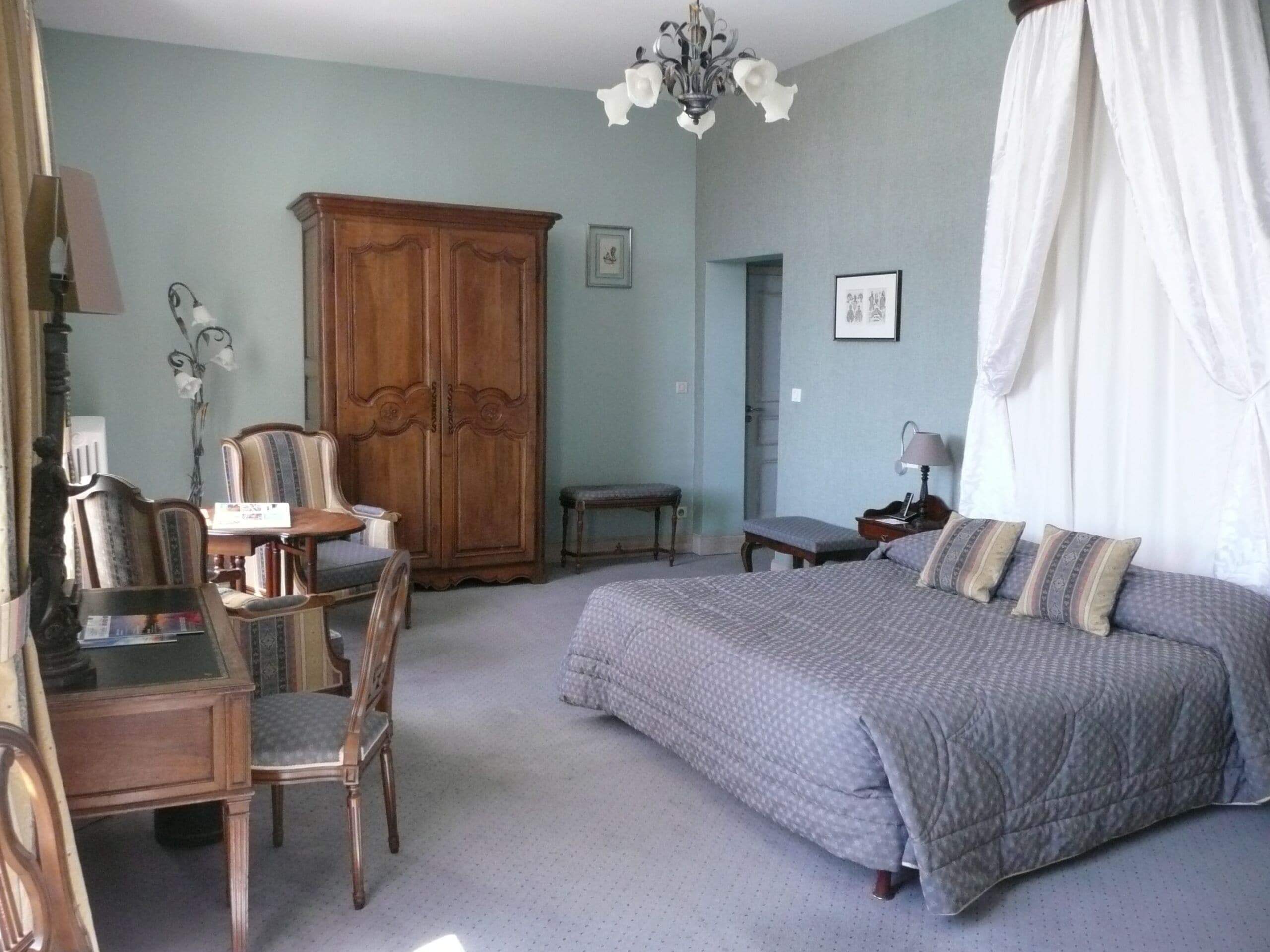 Ein Schlafzimmer mit Bett, Schreibtisch, Stuhl, Kleiderschrank und einer Kandelaber.