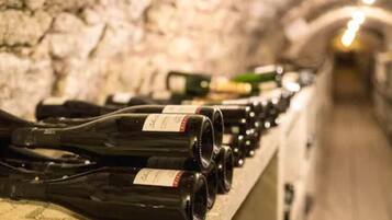 A row of wine bottles on a shelf in a dimly lit, stone-walled cellar.