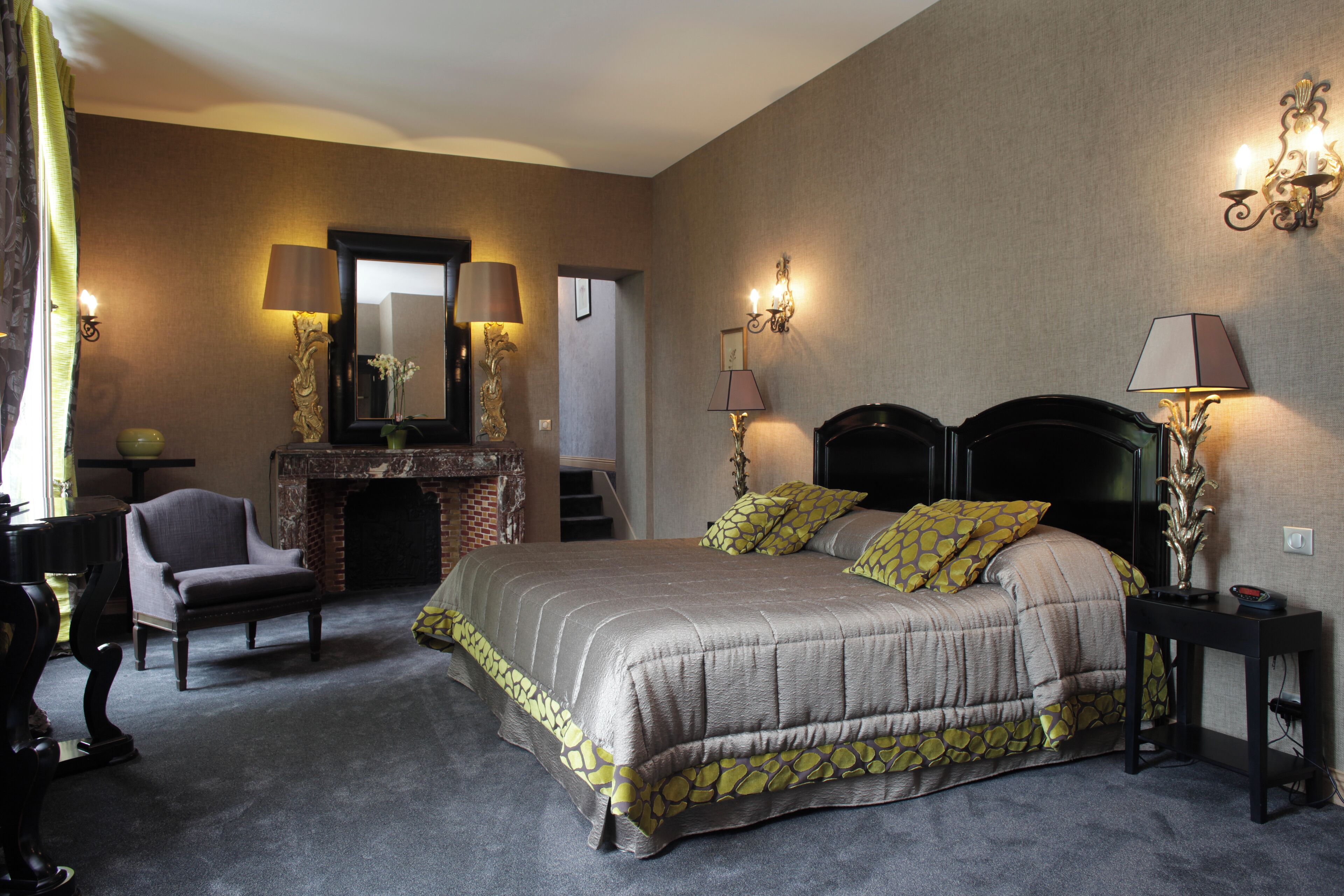 Ein Schlafzimmer mit einem großen Bett, einem Sessel, einem Kamin und Wandleuchten.