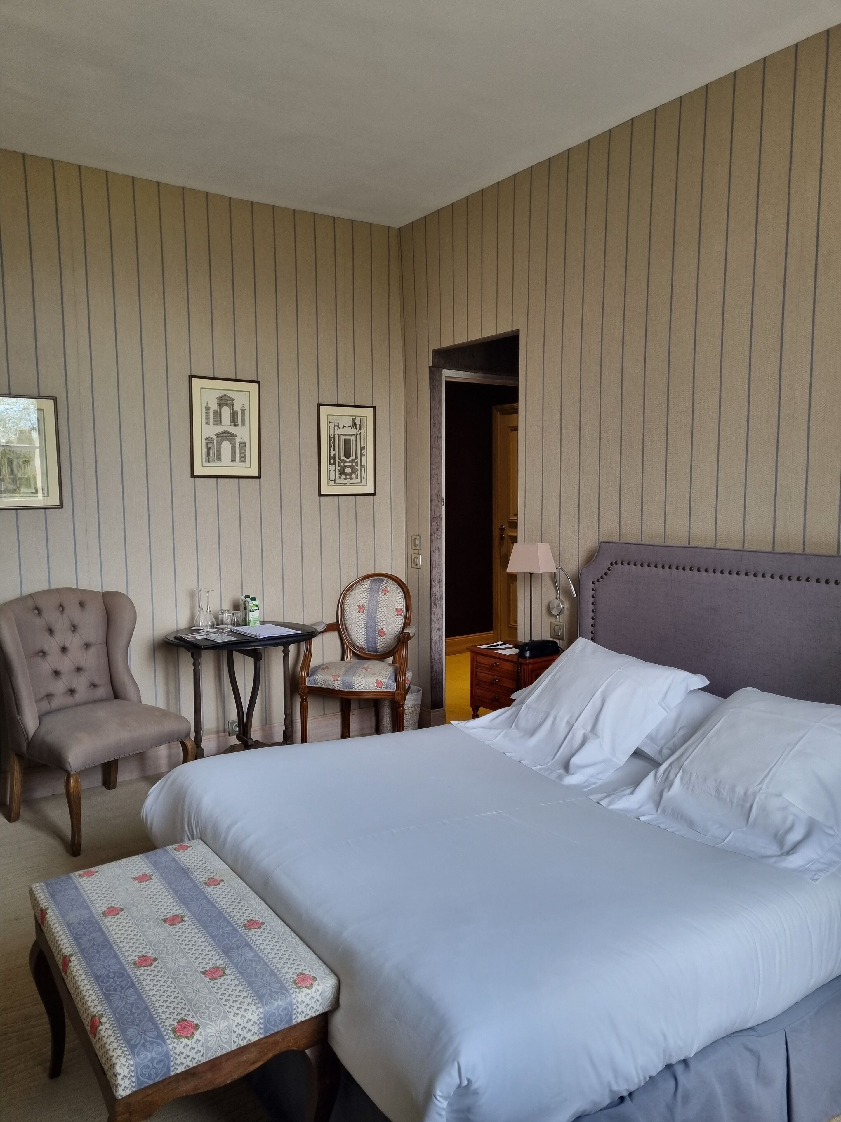 Ein Hotelzimmer mit einem großen Bett, einem Sessel, einem kleinen Tisch und gerahmten Bildern an der Wand.
