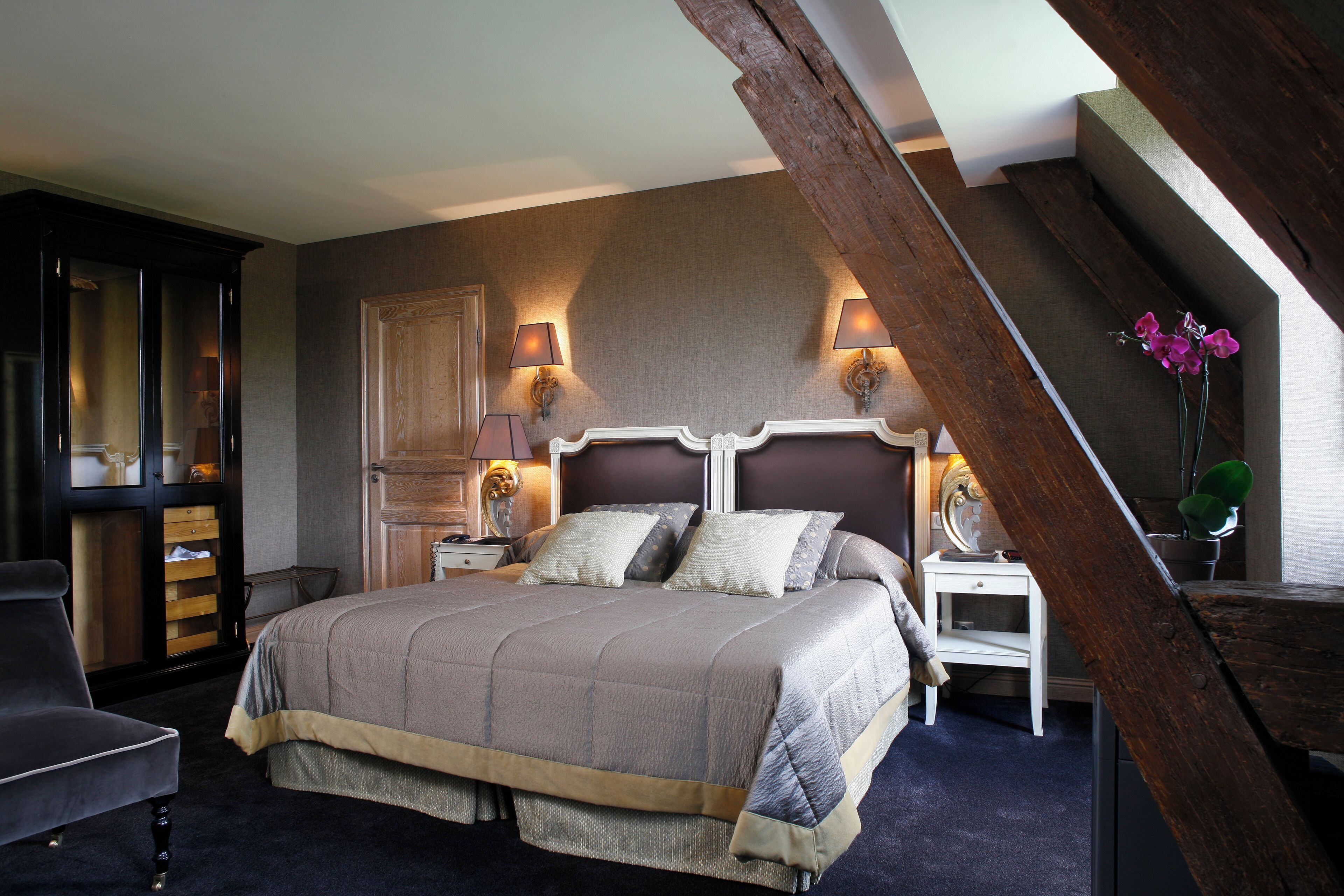 A bedroom with a large bed, two bedside tables with lamps, a wooden wardrobe, and a chair.