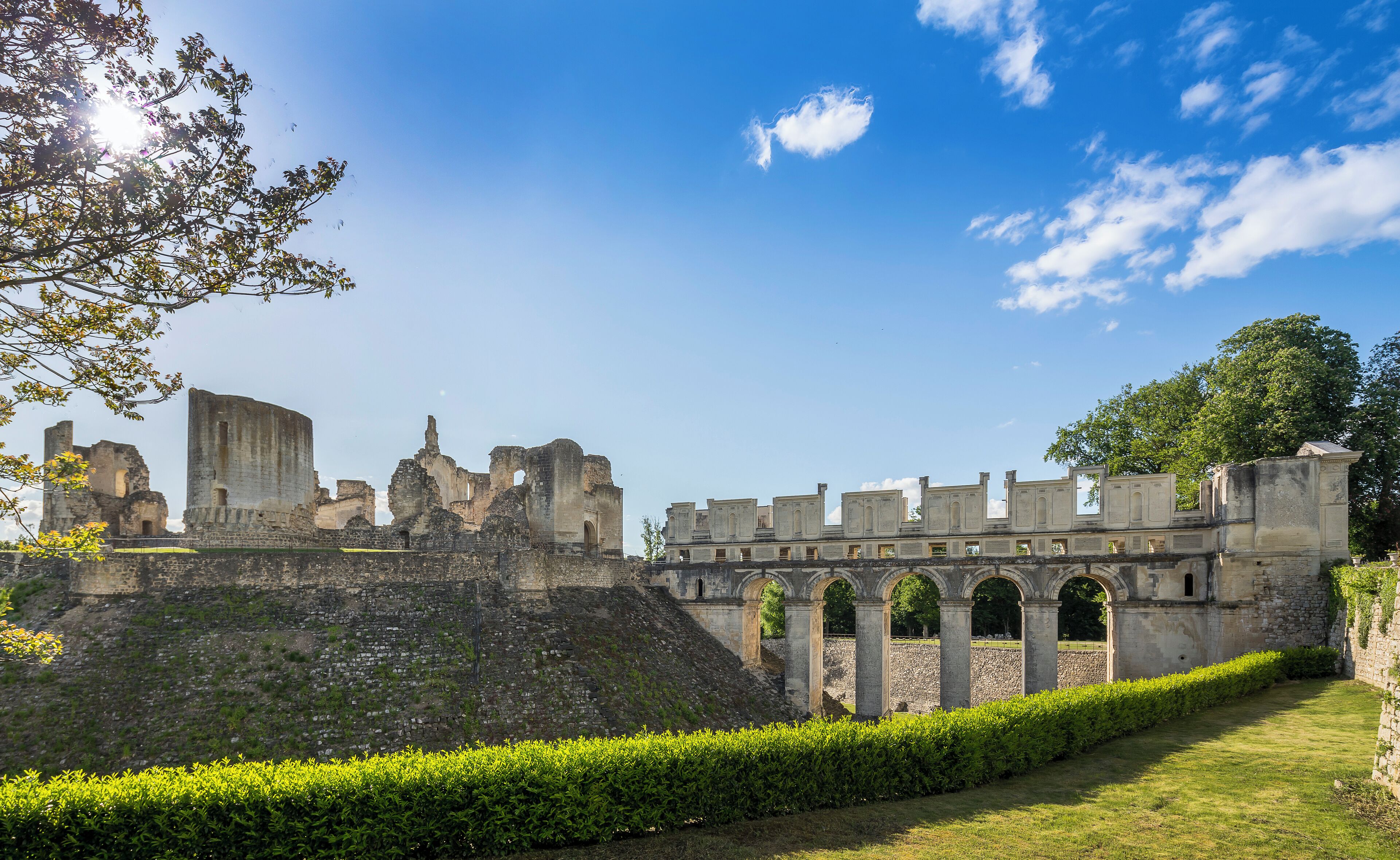A historic stone structure with arches and ruins, surrounded by well-maintained hedges and grass.