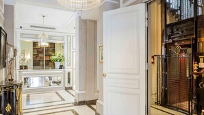A grand hallway with a marble floor, a white door, and a black gate leading to a room. - Hôtel Bradford Elysées – Astotel (Paris)