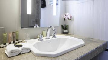 Une salle de bain avec un lavabo blanc, deux robinets, un miroir et une orchidée en pot.