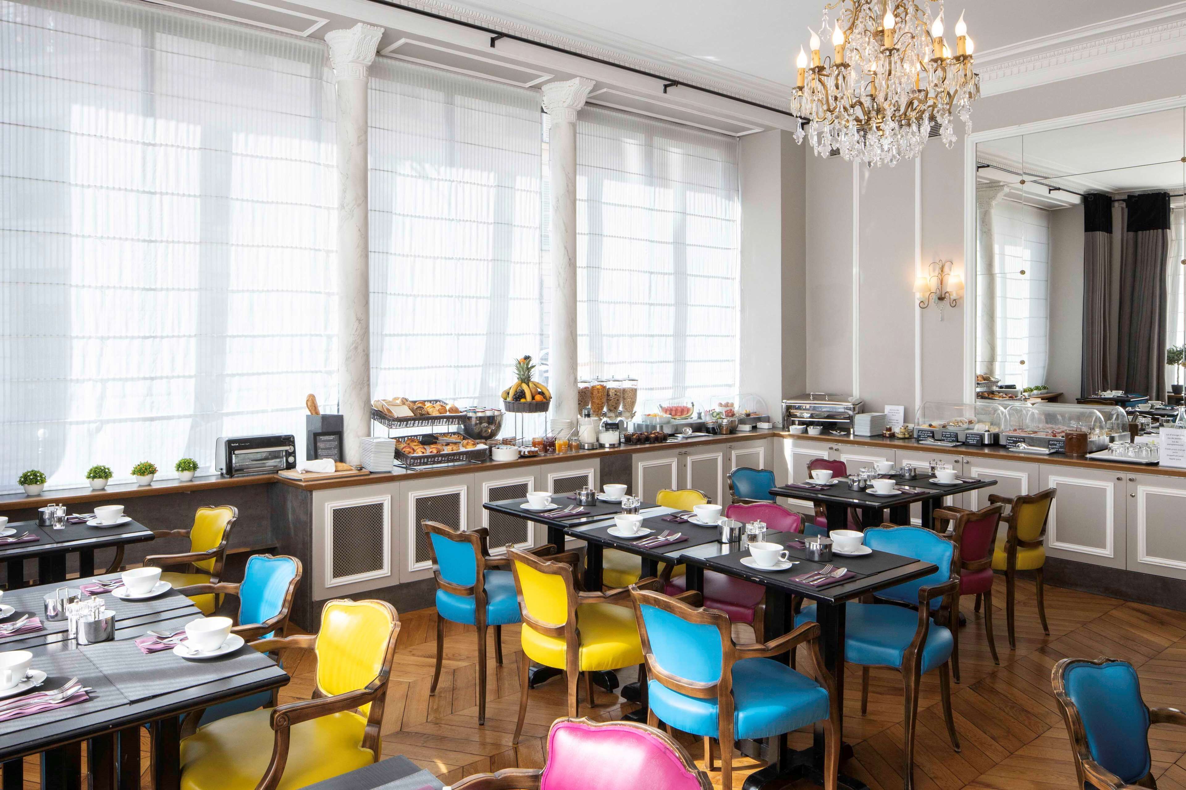 A dining area with multiple tables and chairs, a buffet with various food items, and a chandelier.