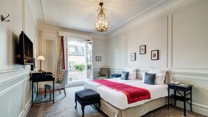 A hotel room with a large bed, a desk with a lamp, a chair, and a view of the outdoors. - Hôtel Bradford Elysées   – Astotel (Paris)