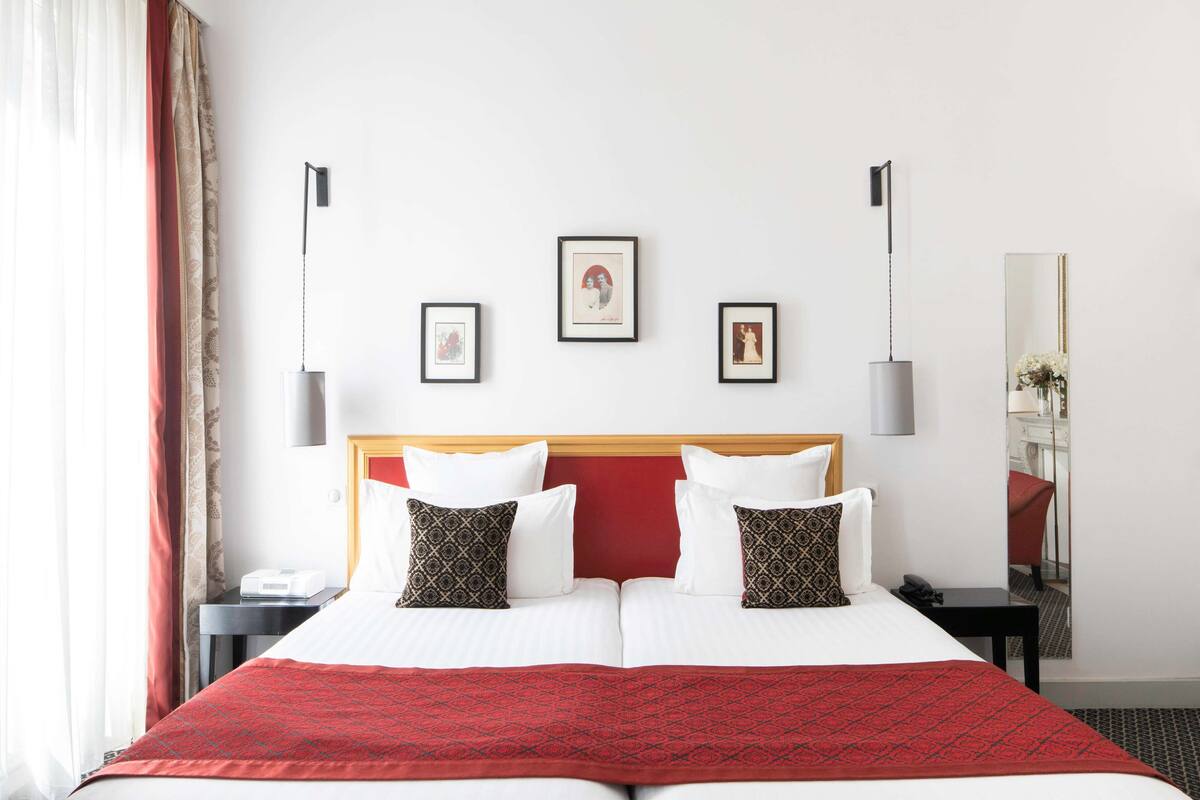 A hotel room with a large bed, two bedside tables, a nightstand, a mirror, and three framed pictures on the wall.
