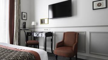 A hotel room with a bed, a desk, a chair, a television, and a framed picture on the wall.