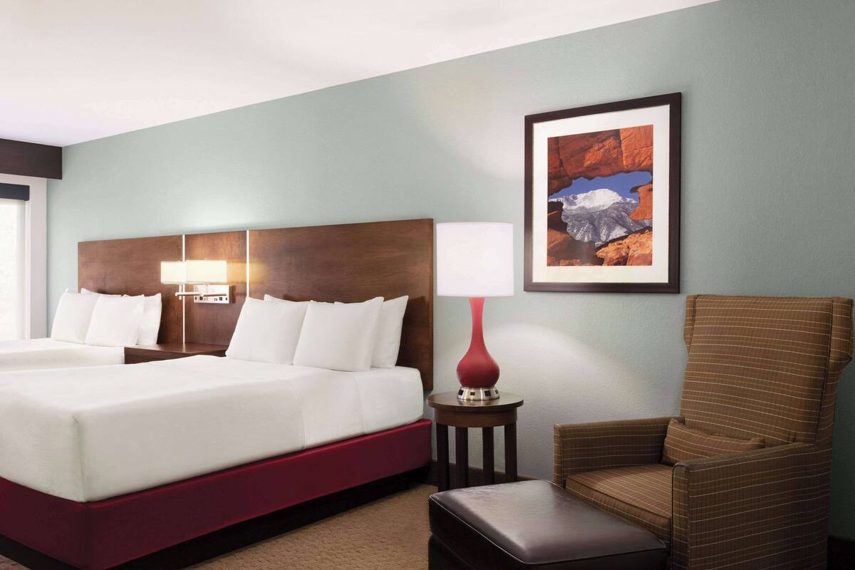 A hotel room with a large bed, a nightstand with a lamp, a chair, and a framed picture on the wall.