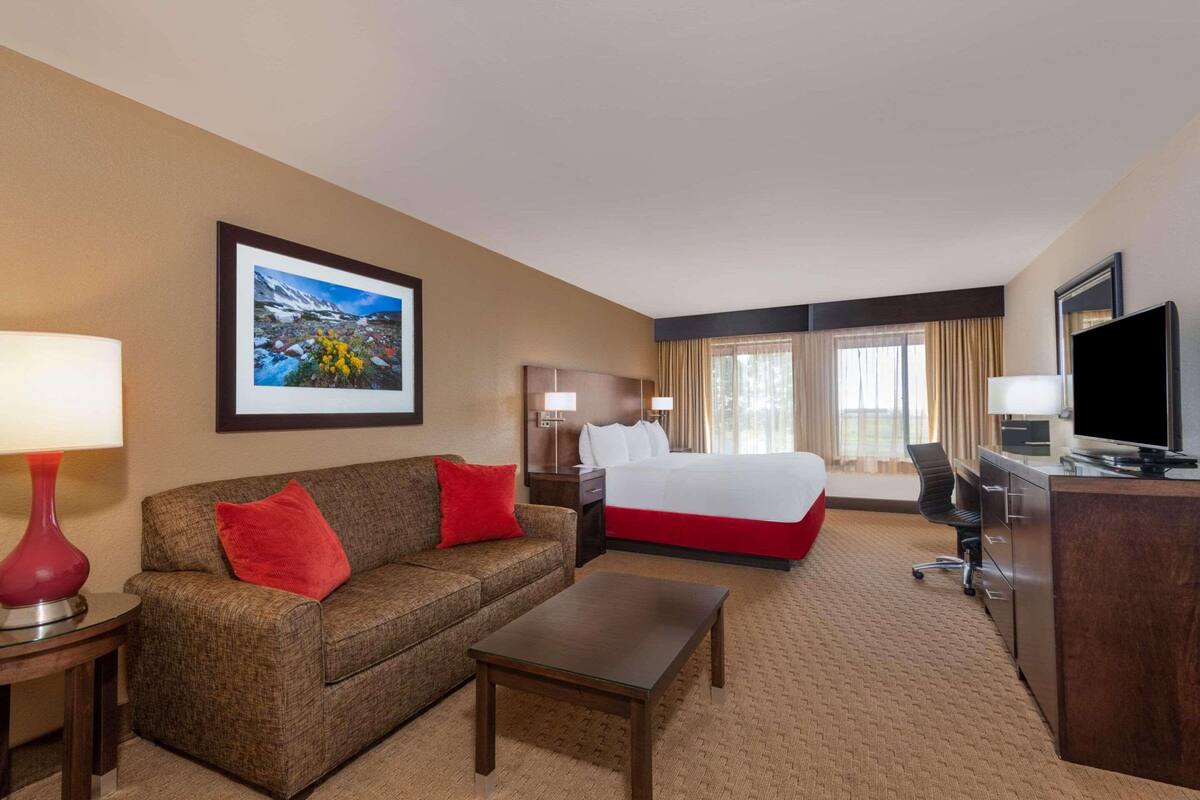 A hotel room with a bed, a sofa, a coffee table, a desk, a TV, and a window with curtains.