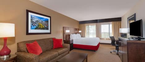A hotel room with a bed, a sofa, a coffee table, a desk, a TV, and a window with curtains.