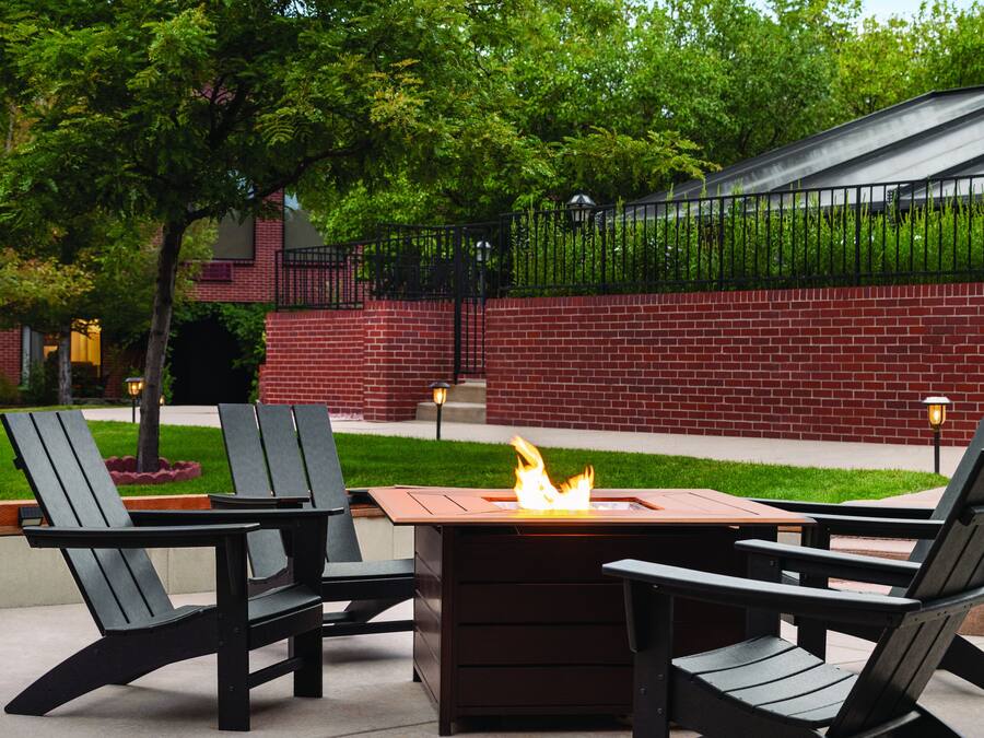 A patio area with a fire pit table and four Adirondack chairs.