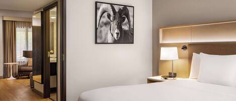 A hotel room with a large bed, a nightstand with a lamp, a framed picture on the wall, and a view of the hallway.