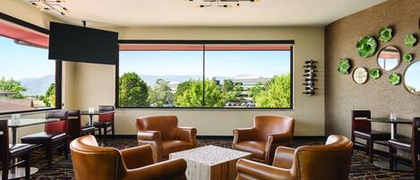 Habitación de hotel con sillones de cuero, una mesa, un televisor y un amplio ventanal con vistas a la ciudad.