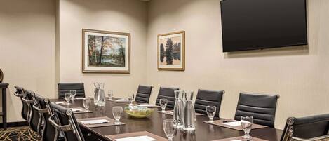 A conference room with a long table, chairs, a TV, and framed pictures on the wall.