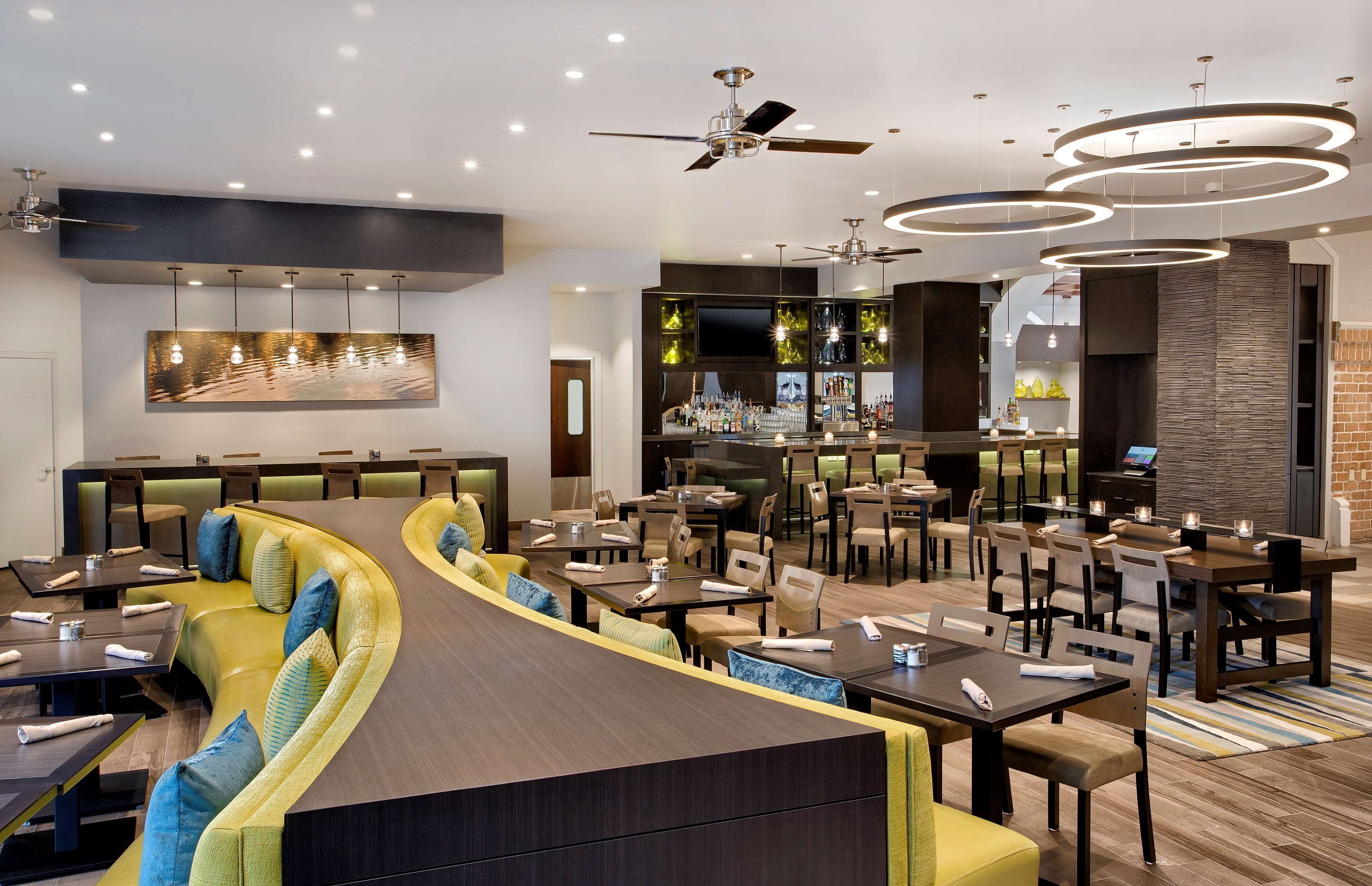 Un restaurante moderno con una zona de asientos curva, varias mesas y una barra con una pantalla de televisión.
