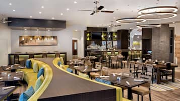 Un restaurante moderno con una zona de asientos curva, varias mesas y una barra con una pantalla de televisión.