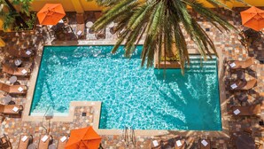 A rectangular swimming pool with clear blue water, surrounded by lounge chairs and orange umbrellas.