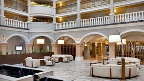 A spacious lobby with multiple seating areas, a central water feature, and a high ceiling with balconies.