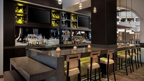 A bar area with a long counter, multiple shelves with bottles, and bar stools.