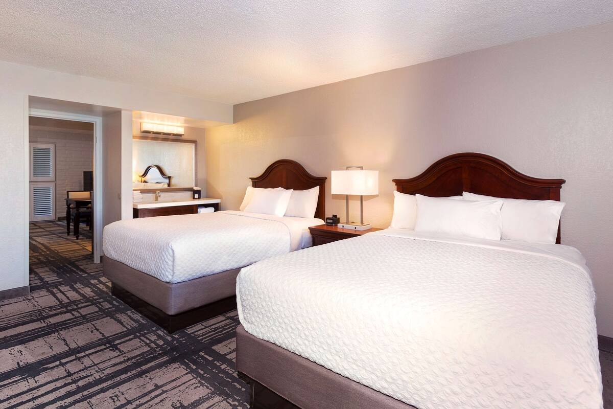 A hotel room with two beds, a desk, and a chair.