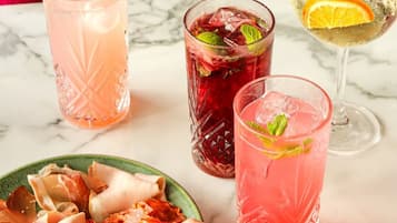 A table with three drinks, a plate of cured meats, and a glass of wine.