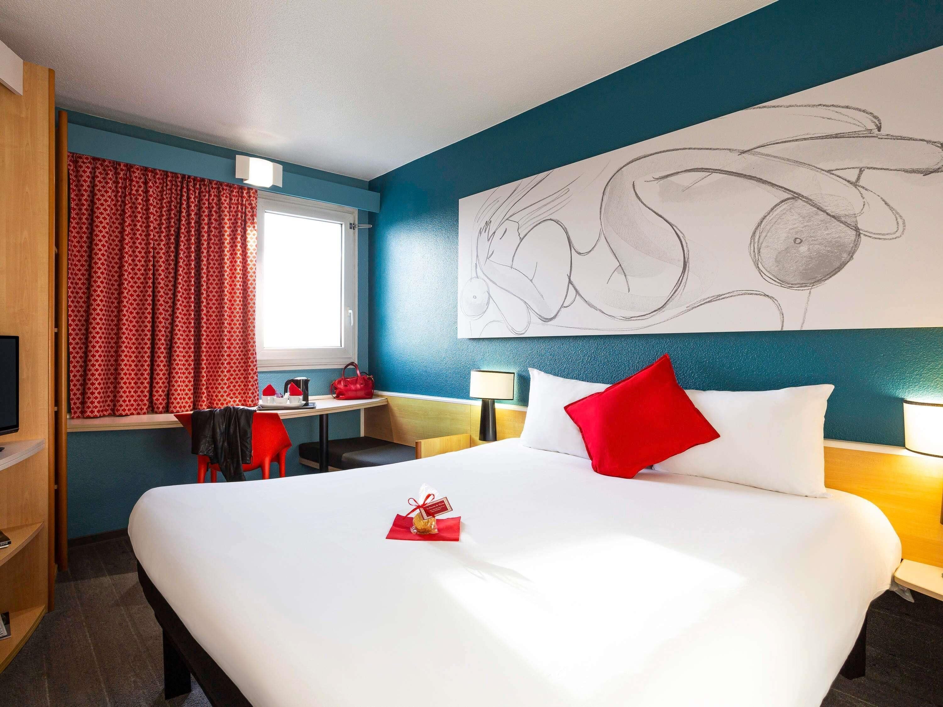 A hotel room with a large bed, a desk with a chair, a TV, and a window with curtains.
