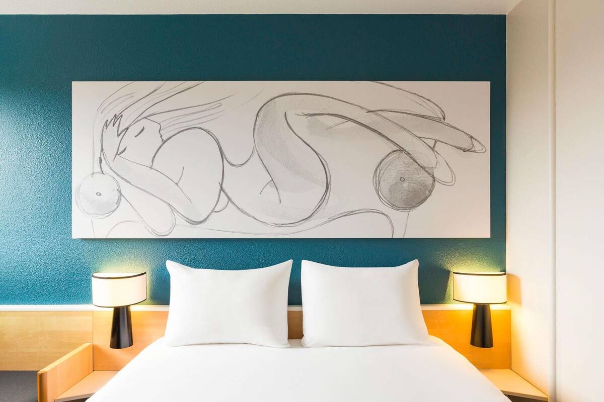 A hotel room with a large bed, two bedside lamps, and a wall-mounted abstract artwork.