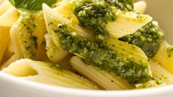 A bowl of pasta with pesto sauce and basil leaves.