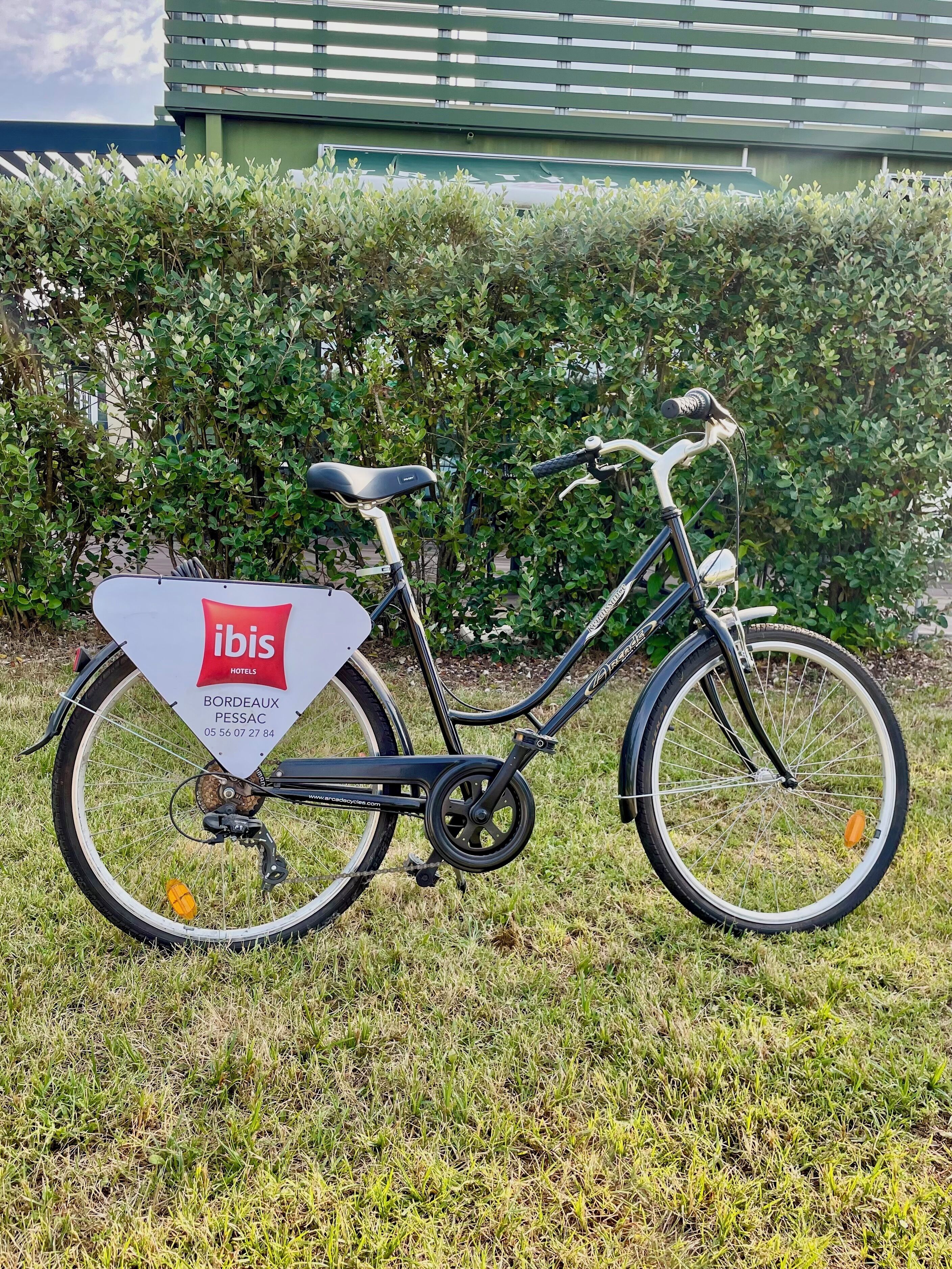 A bicycle parked on grass with a sign indicating 'ibis HOTELS BORDOAX PESSAC'.