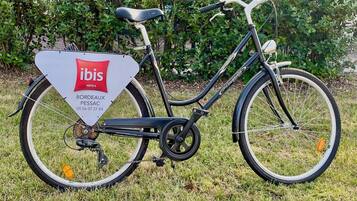 Ein Fahrrad auf Gras, mit einem Schild, auf dem 'ibis HOTELS BORDOAX PESSAC' steht.
