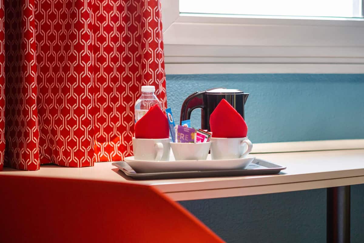 A breakfast setup with two cups, a bottle, and a kettle on a tray by a window.
