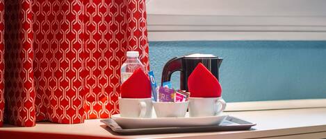 A breakfast setup with two cups, a bottle, and a kettle on a tray by a window.