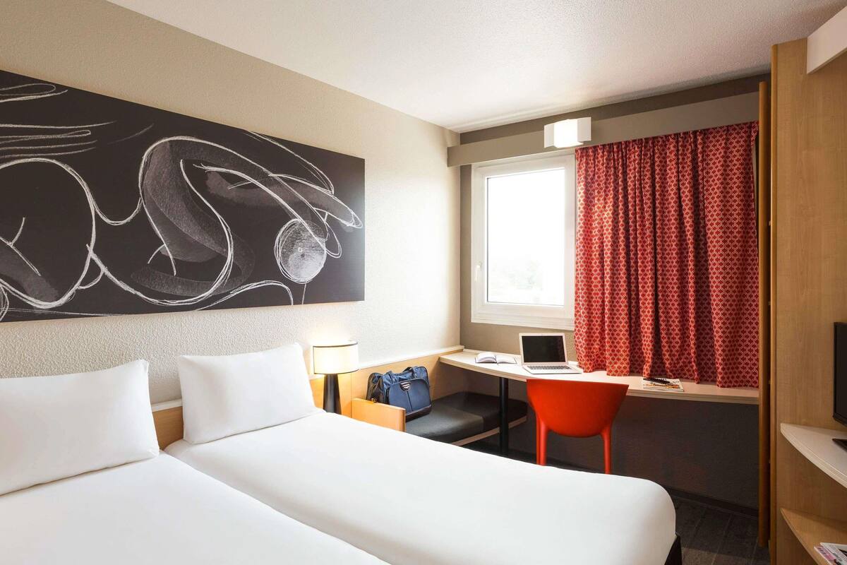 Habitación de hotel con cama, escritorio con una computadora portátil, una silla, una lámpara y un cuadro abstracto grande en la pared.