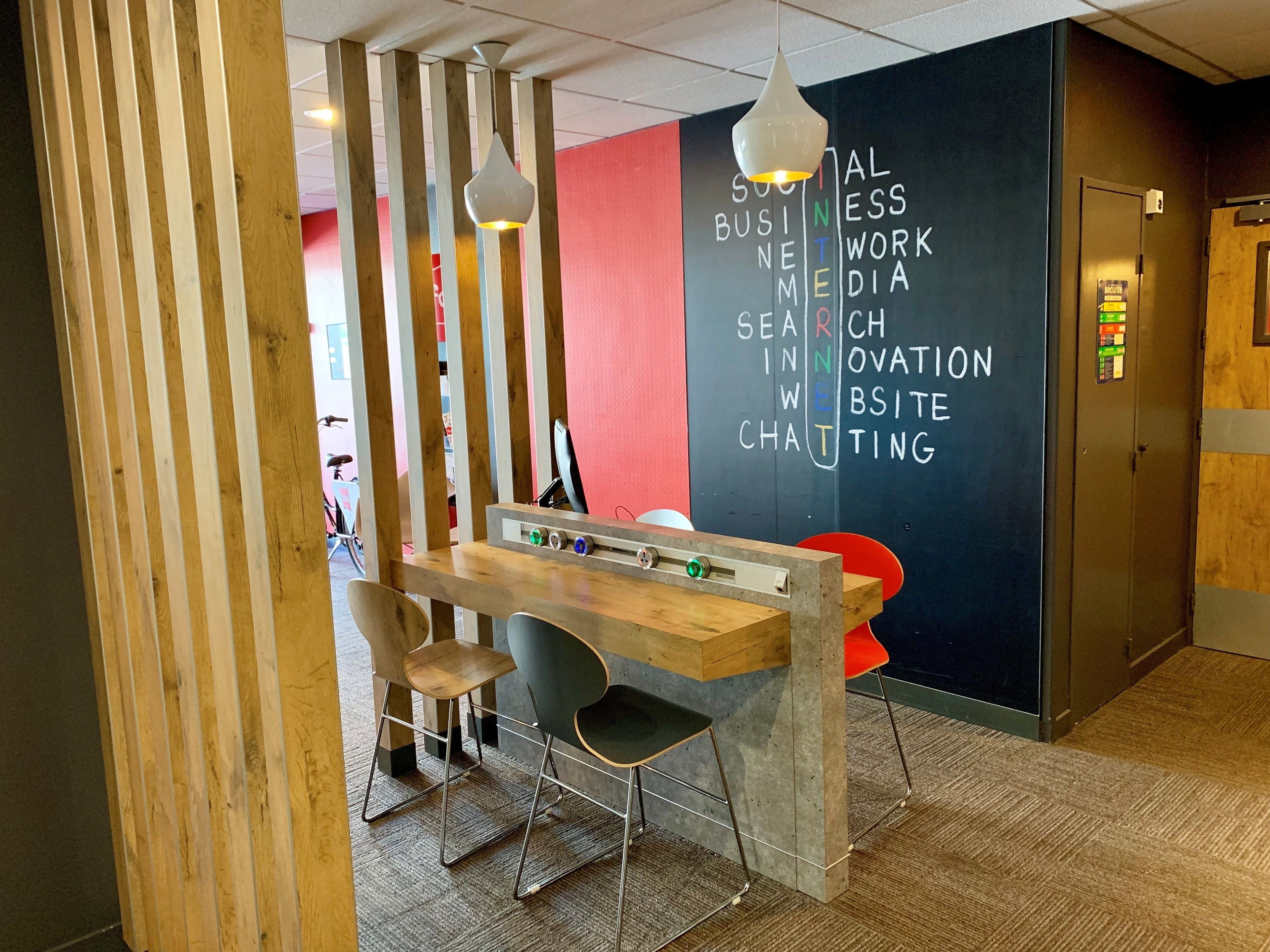 A modern workspace with a wooden desk, two chairs, and a blackboard with business-related words.