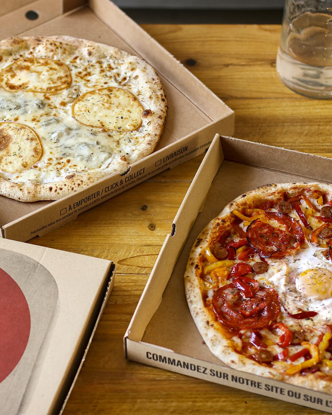 Three pizza boxes on a wooden table.
