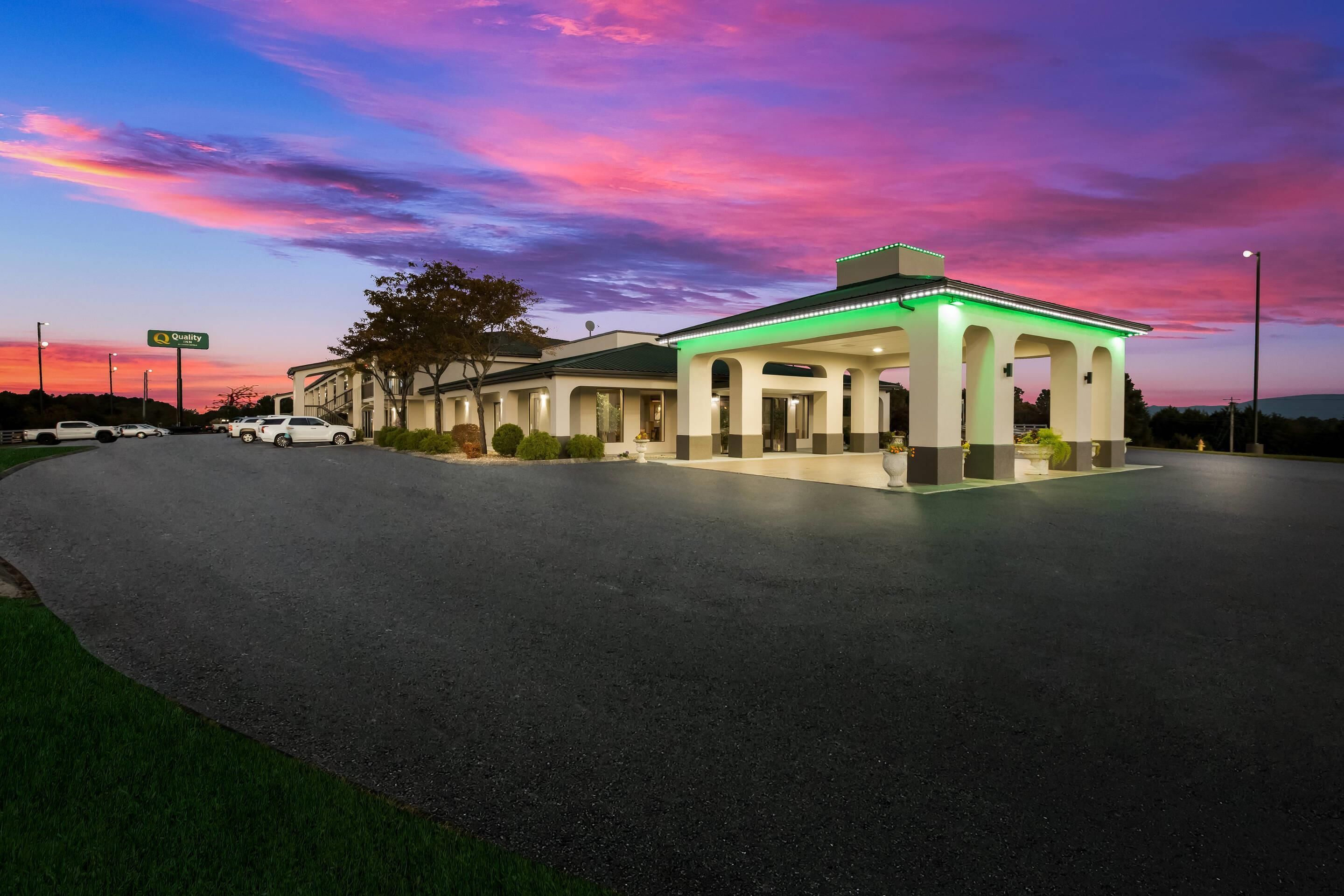 A hotel with a covered outdoor area, a parking lot, and a sign indicating a 'Quality' service.