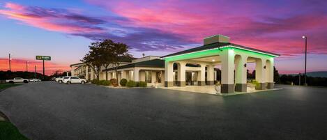 A hotel with a covered outdoor area, a parking lot, and a sign indicating a 'Quality' service.
