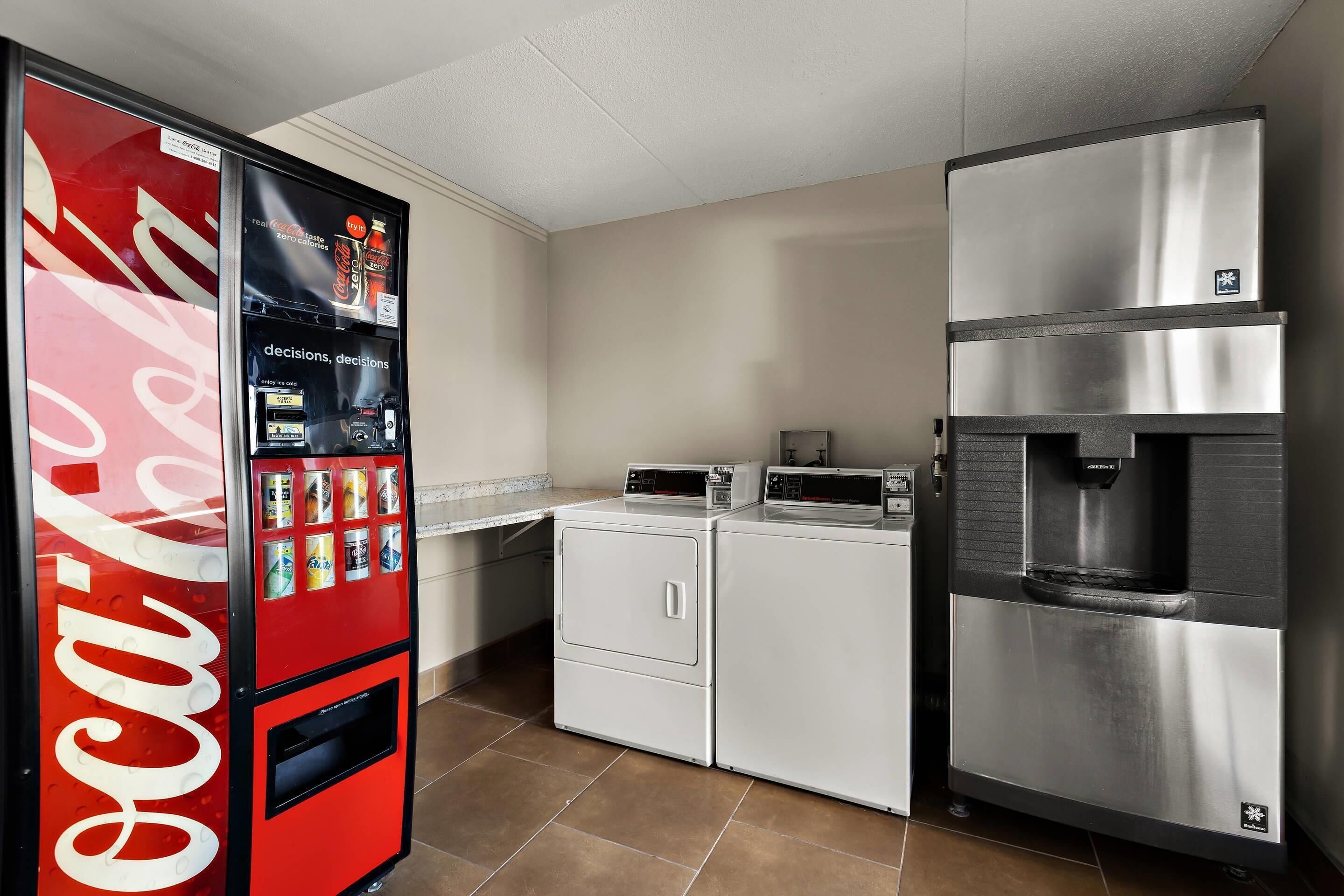 A kitchen with a Coca-Cola vending machine, a microwave, a refrigerator, and a washing machine.