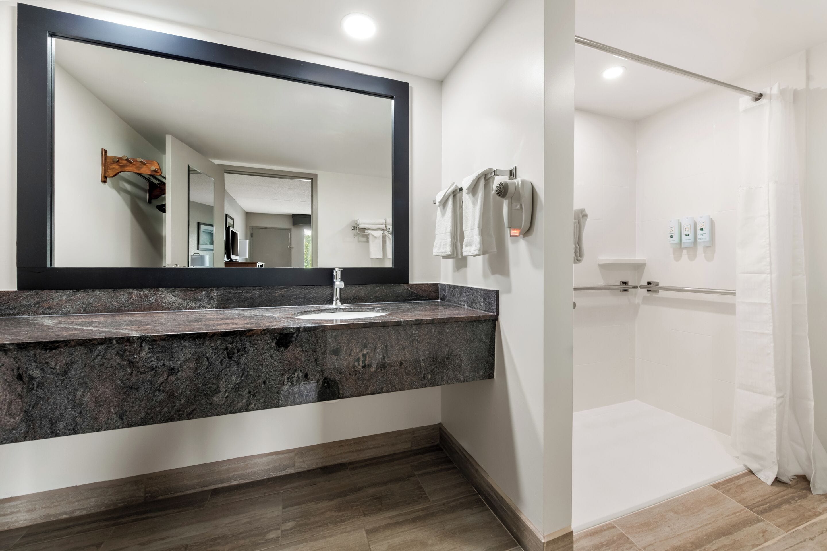 A modern bathroom with a granite countertop, a large mirror, a shower with a glass door, and a towel rack.