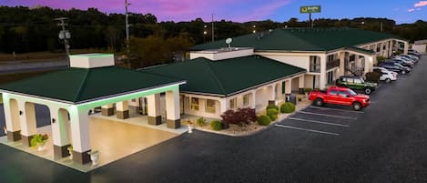 A motel with a green roof, a parking lot, and a sign that reads "Quality."
