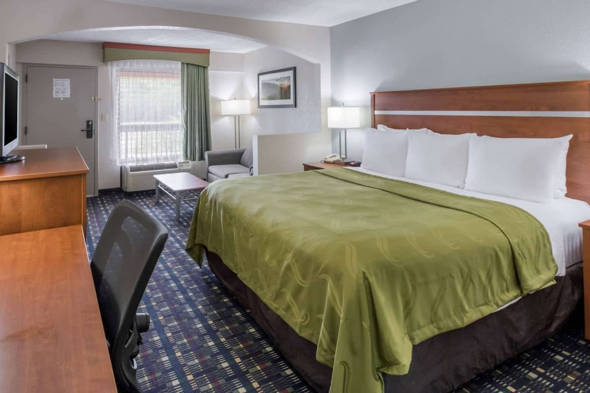 A hotel room with a bed, a desk, a chair, a television, and a window with curtains.